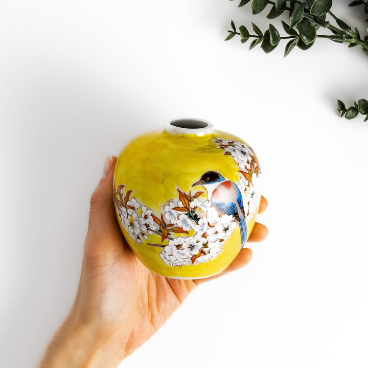 Bright yellow vase adorned with delicate cherry blossoms and a colorful bird, capturing the essence of spring in a beautifully painted design.