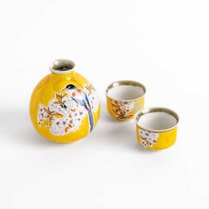 Bright yellow sake set featuring a floral design with a bird perched on cherry blossoms, including a round bottle and two matching cups, perfect for spring celebrations.
