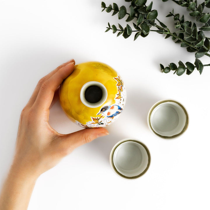 Bright yellow sake set featuring a floral design with a bird perched on cherry blossoms, including a round bottle and two matching cups, perfect for spring celebrations.