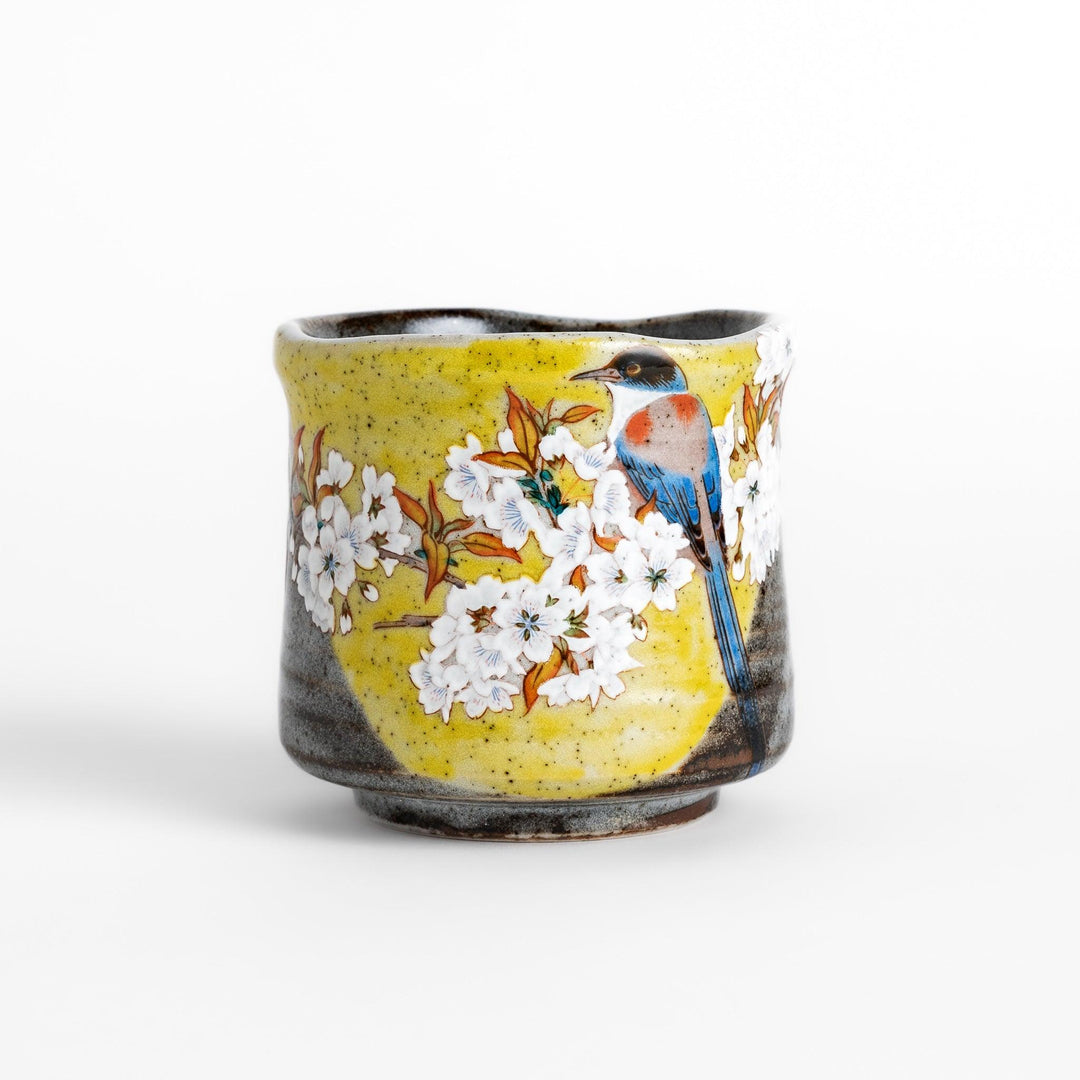 Tea Cup featuring a bird perched on blooming sakura flowers, set against a yellow and gray background.