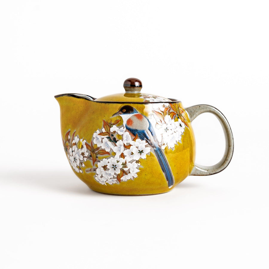 Yellow ceramic teapot with a beautiful bird and flower design, featuring a smooth sheen and secure lid, perfect for serving tea.