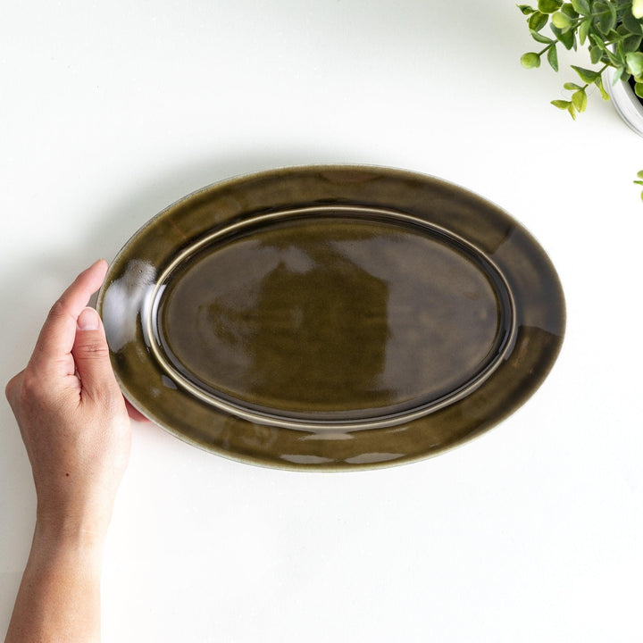 Sleek, dark brown or olive colored oval dinner plate with a glossy finish, simple and minimalist.