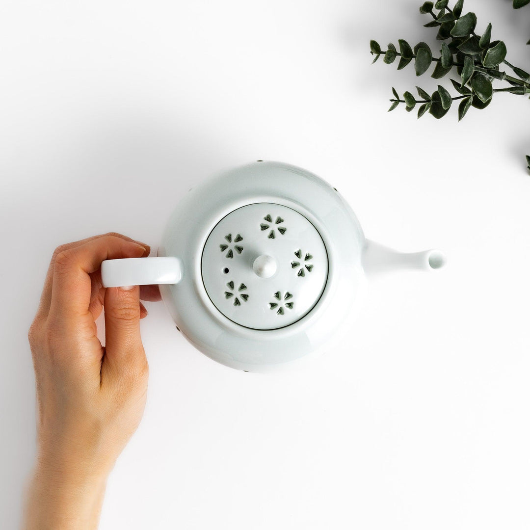 Elegant teapot with delicate petal-shaped cutouts, creating a soft glow through the porcelain, complemented by a pointed lid and smooth handle for a refined tea experience.