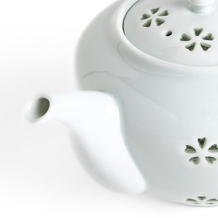 Elegant teapot with delicate petal-shaped cutouts, creating a soft glow through the porcelain, complemented by a pointed lid and smooth handle for a refined tea experience.