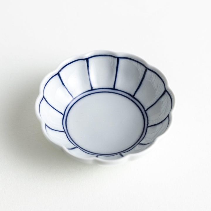 A small white porcelain condiment bowl with delicate blue or red lines radiating from the center, creating a simple yet elegant design.