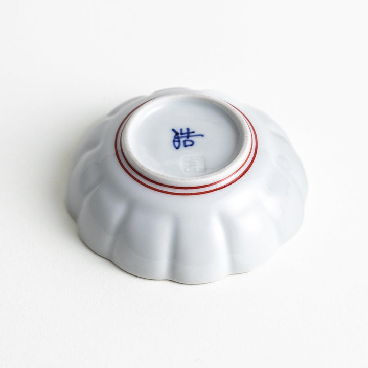 A small white porcelain condiment bowl with delicate blue or red lines radiating from the center, creating a simple yet elegant design.