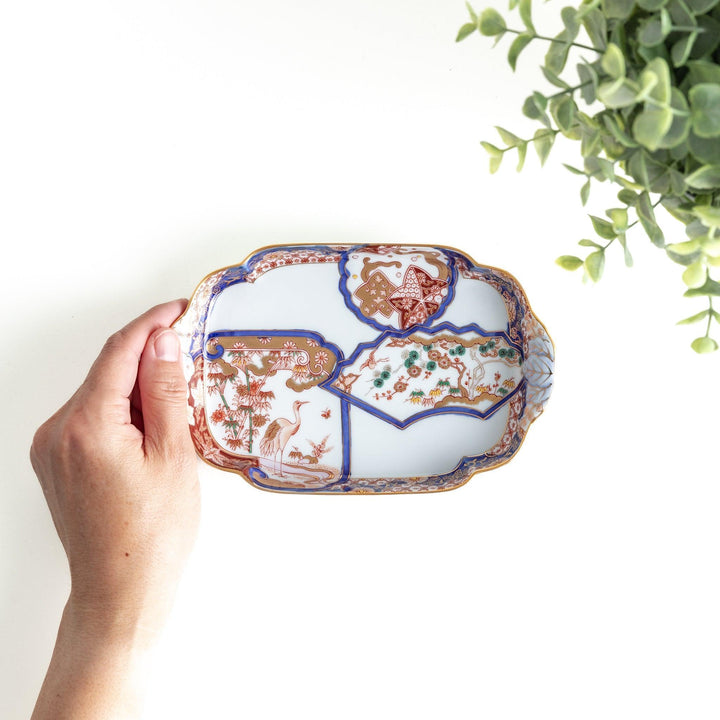 A rectangular salad plate with handles, decorated with scenes of cranes and trees in a traditional Japanese style, bordered by intricate red, blue, and gold patterns.
