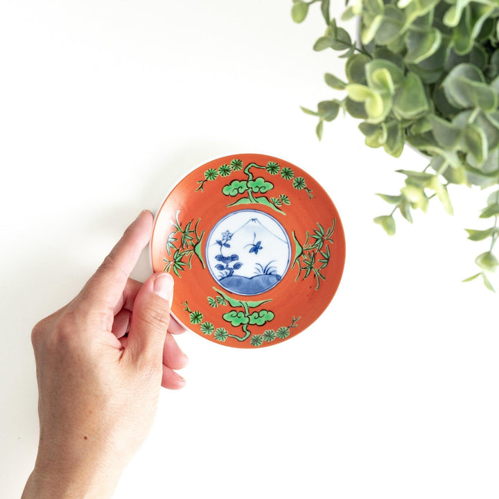 Round plate with an orange background, green leaves, and a Mount Fuji scene.