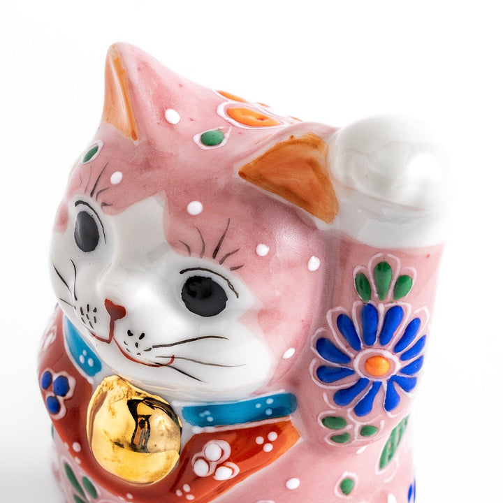 Charming pink blossom Maneki Neko figurine, adorned with colorful floral patterns and a golden bell, symbolizing good luck and prosperity with a cheerful waving gesture.
