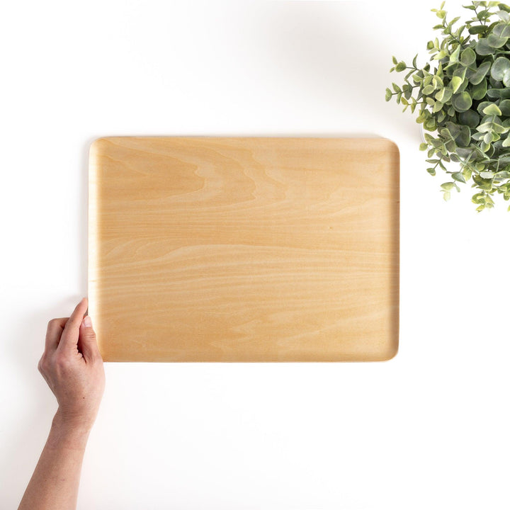 Hand holding a rectangular wooden tray with a light brown finish, a versatile serveware piece for carrying food, drinks, or decorative items with a touch of natural warmth.
