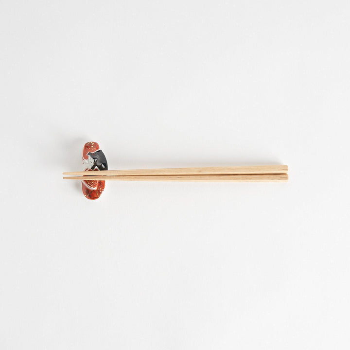 A ceramic chopstick rest shaped like a Japanese princess, painted in orange with floral accents.