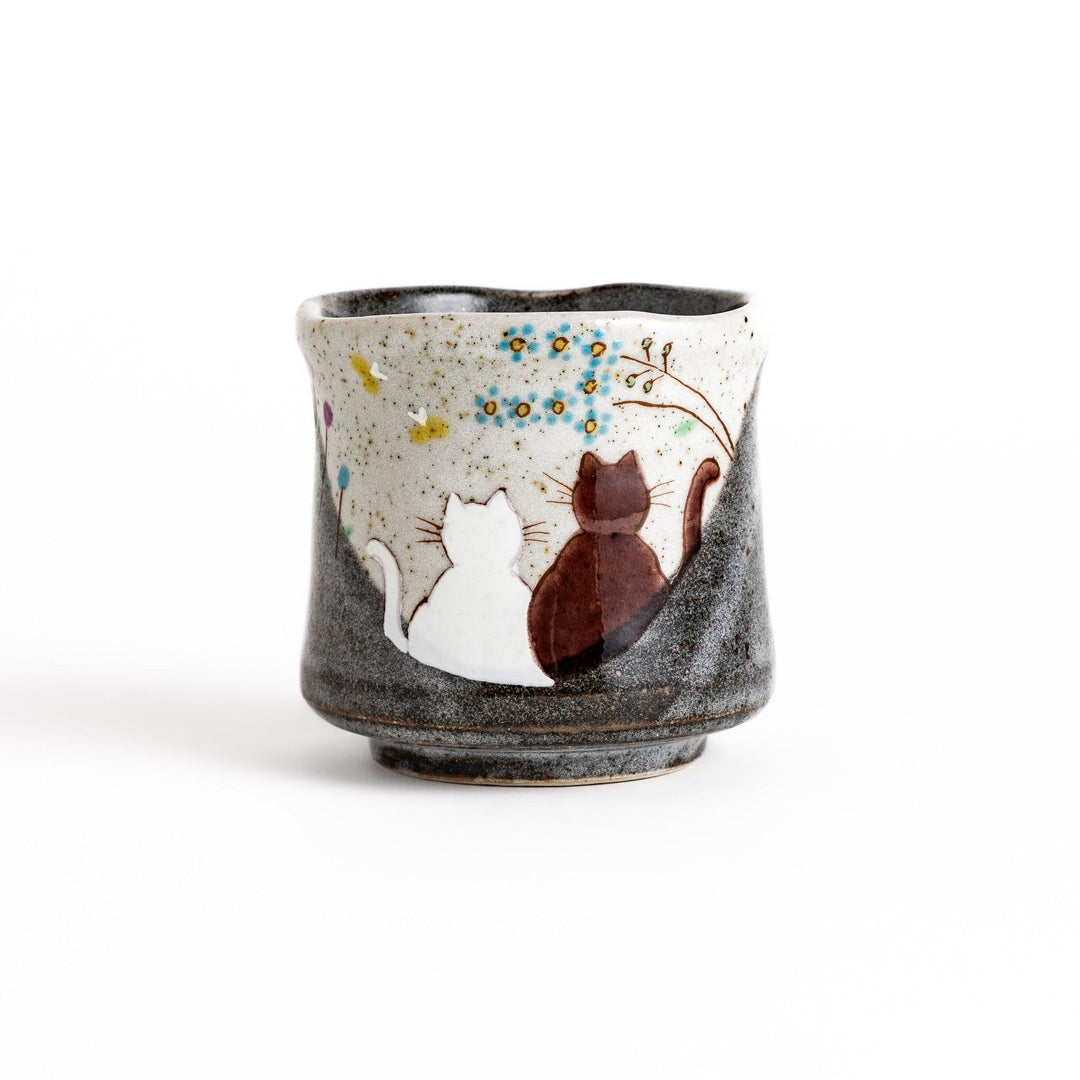 Charming ceramic teacup featuring two cats gazing at small flowers, with a unique speckled glaze and a comfortable shape for holding.