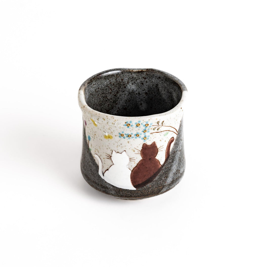 Charming ceramic teacup featuring two cats gazing at small flowers, with a unique speckled glaze and a comfortable shape for holding.