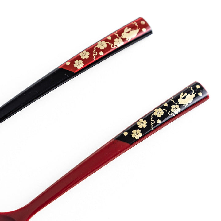 A set of two coffee spoons, one red and one black, with gold floral designs on the handles.