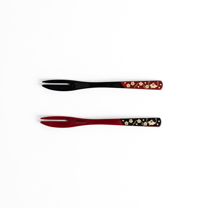 A set of two dessert forks, one red and one black, with rabbit designs on the handles.