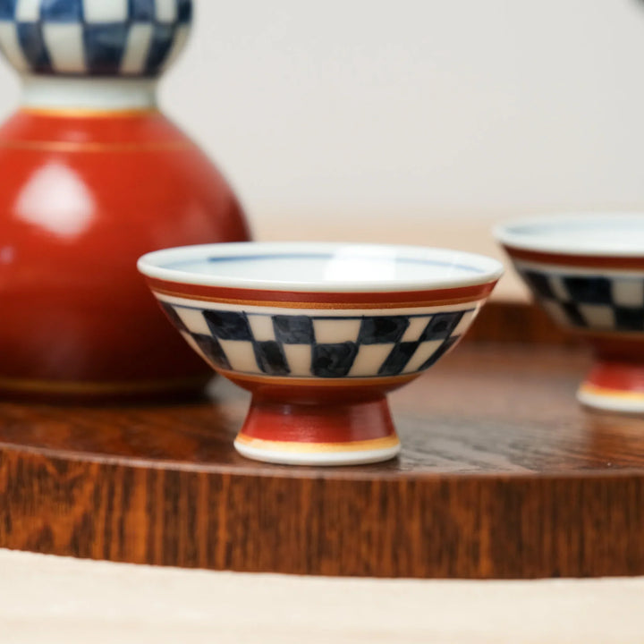 Japanese sake cup with red base and blue checkered design, crafted in ceramic for enjoying traditional warm or cold sake.