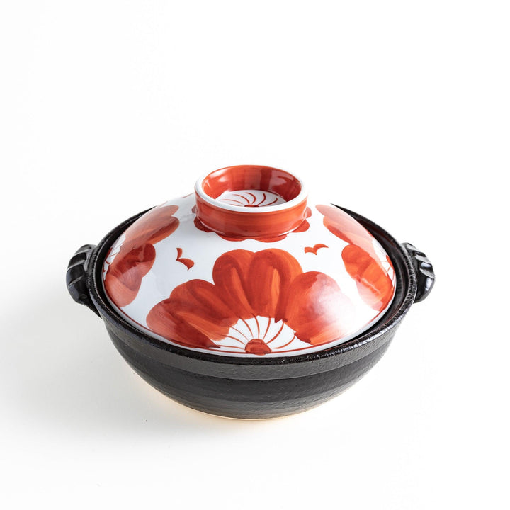 A beautifully crafted donabe with a vibrant red floral pattern on the lid, perfect for serving various hot dishes.