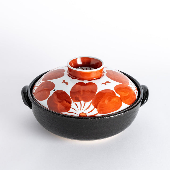 A beautifully crafted donabe with a vibrant red floral pattern on the lid, perfect for serving various hot dishes.