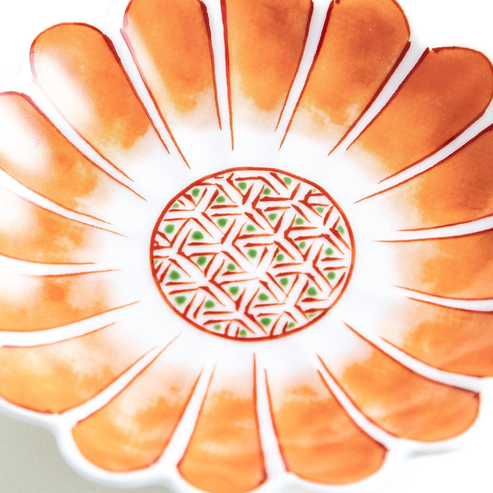 A small, scalloped-edge porcelain dish with orange chrysanthemum petal designs and a geometric center.