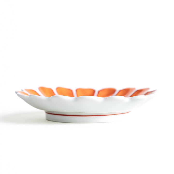 A small, scalloped-edge porcelain dish with orange chrysanthemum petal designs and a geometric center.