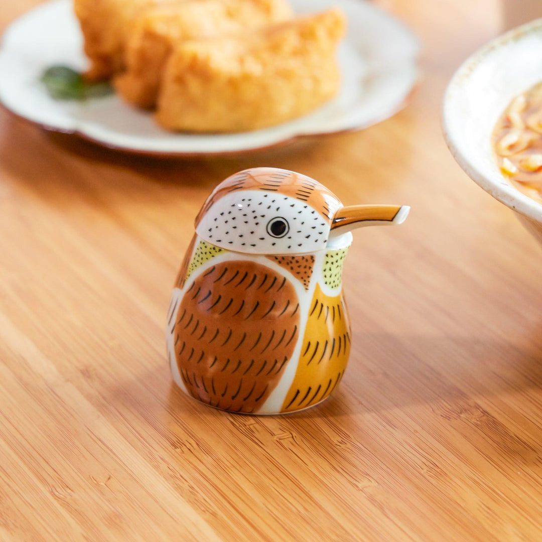 Red Sparrow Soy Sauce Dispenser shaped like a bird, placed on a wooden table beside ramen and inari sushi