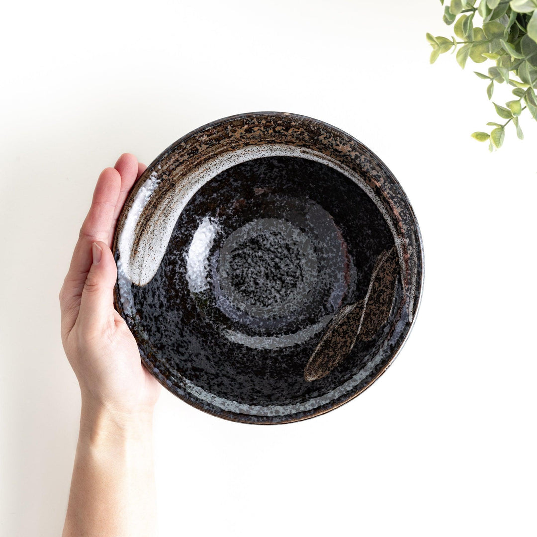 A deep ceramic bowl with a glossy black glaze and irregular brown and speckles.