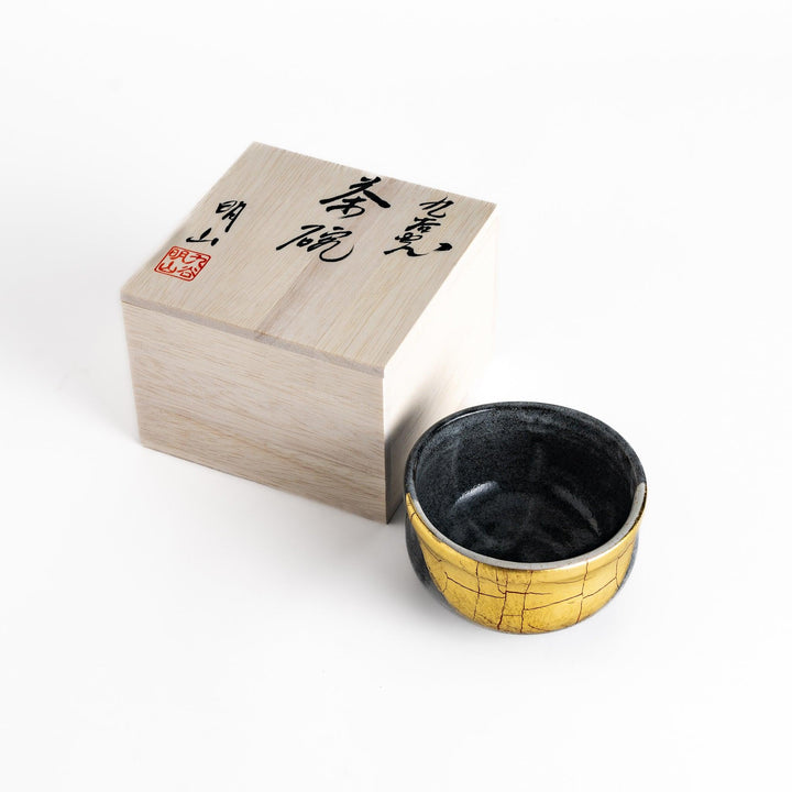 Black matcha bowl with a unique gold-accented crackle glaze, presented in a traditional wooden box, perfect for a special tea ceremony.