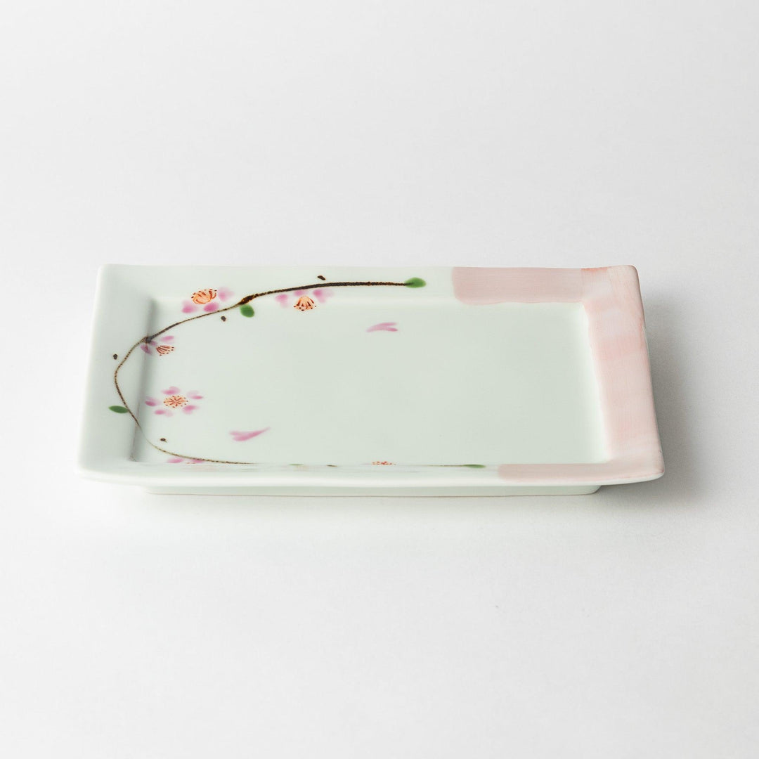 Dessert plate viewed at an angle, showing the pink cherry blossoms and delicate green accents along the edges.