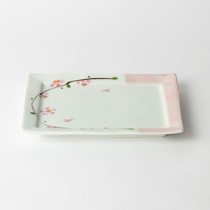 Dessert plate viewed at an angle, showing the pink cherry blossoms and delicate green accents along the edges.