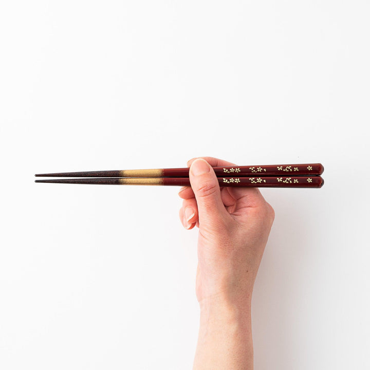Elegant red and brown lacquered chopsticks adorned with delicate gold cherry blossom motifs, featuring a gradient of gold for added sophistication.