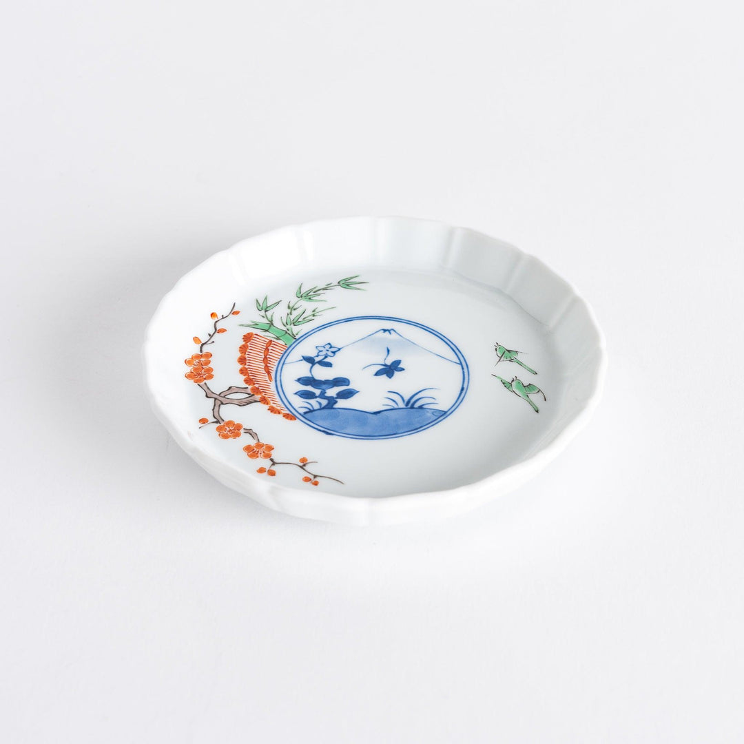 A small round plate with a traditional Japanese design depicting a landscape and floral elements.