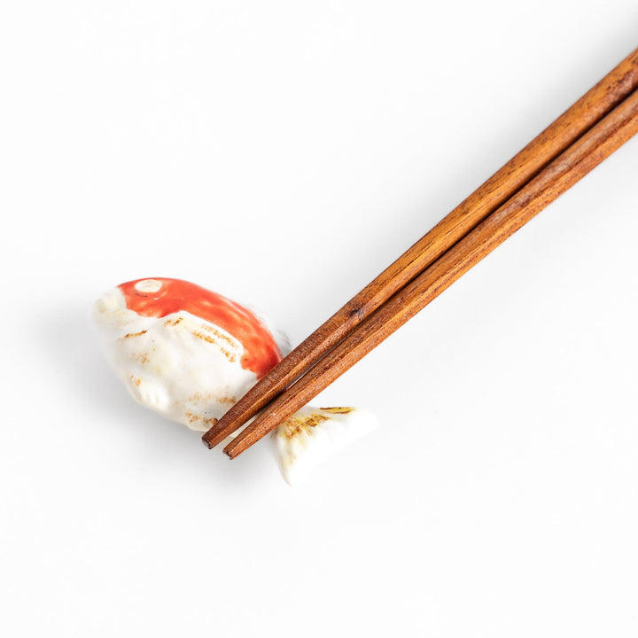 Chopstick rest shaped like a sea bream, intricately painted with red and white hues.