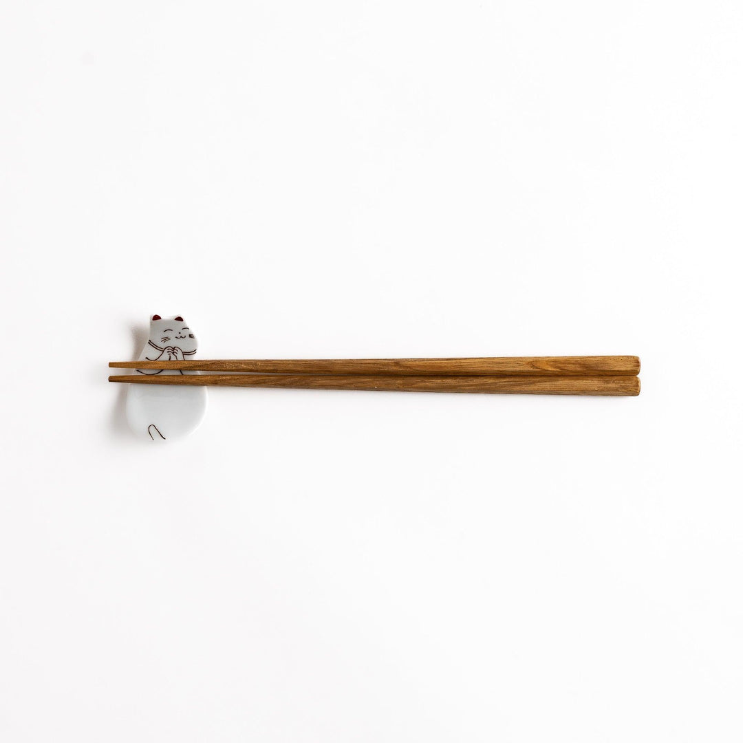 Ceramic sleeping cat-shaped chopsticks rest with chopsticks placed, showcasing its elegant brown and red line art details.