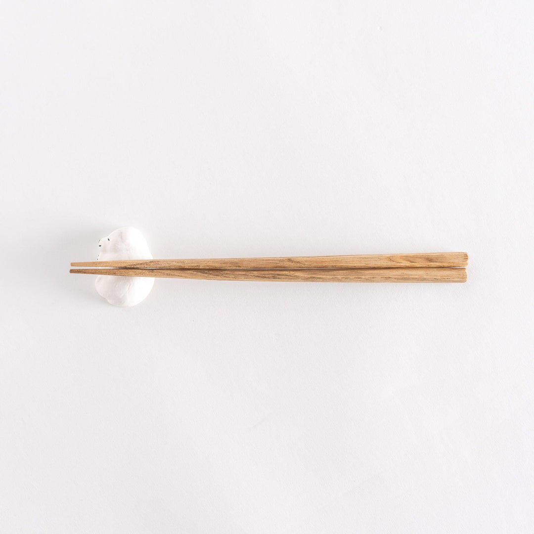Slightly angled view of a chopstick rest in the shape of a sleeping bear, with chopsticks placed on it.