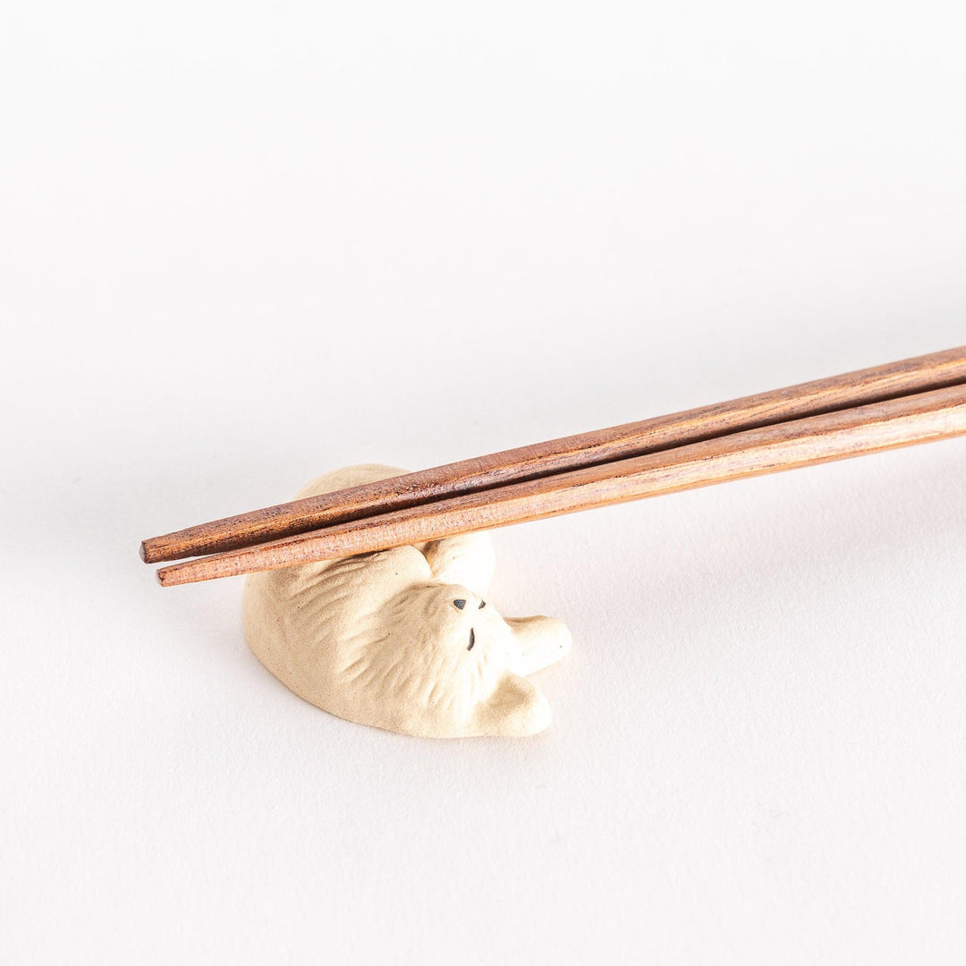 Close-up view of a chopstick rest in the shape of a sleeping cat, with chopsticks resting on it, focusing on the details of the cat’s form.