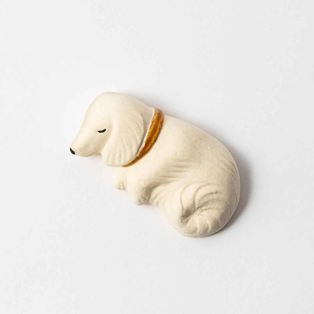 A white ceramic chopstick rest shaped like a sleeping dog, featuring a gold collar.