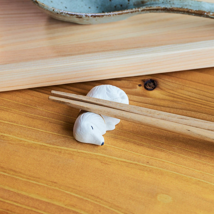 Wooden chopsticks resting on a ceramic chopstick rest shaped like a sleeping white dog.