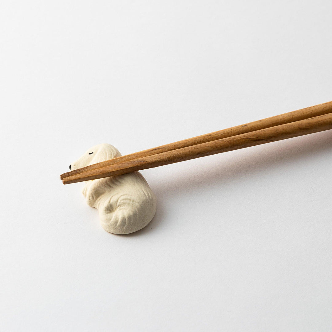 Close-up of a white ceramic sleeping dog chopstick rest with chopsticks resting on its back.