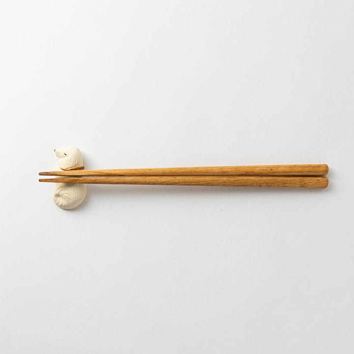 Wide shot of a white ceramic sleeping dog chopstick rest holding chopsticks across its back.