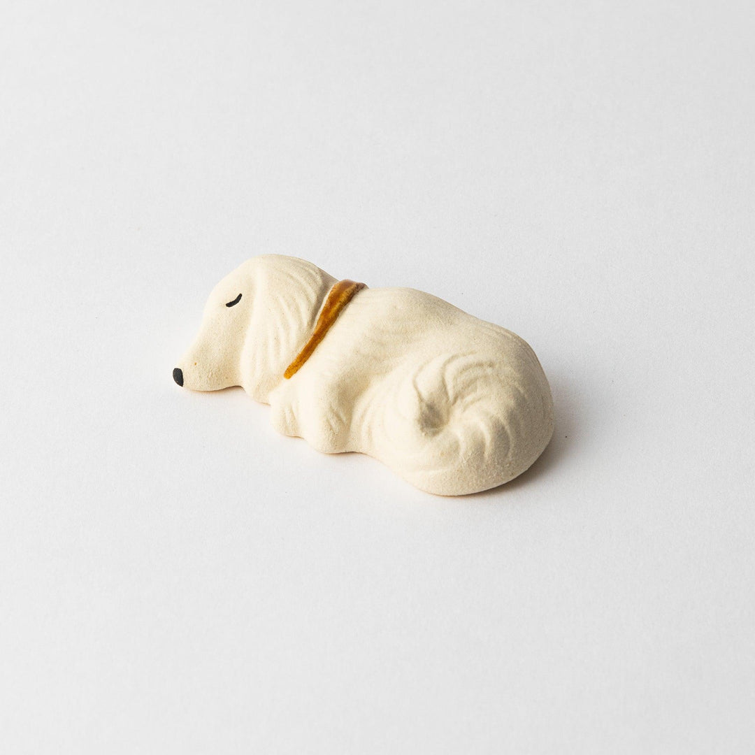 Angled view of a white ceramic sleeping dog chopstick rest, highlighting its soft curves and gold collar.