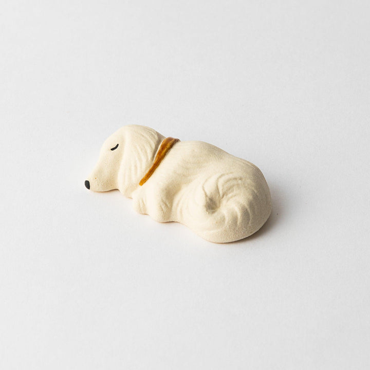Angled view of a white ceramic sleeping dog chopstick rest, highlighting its soft curves and gold collar.