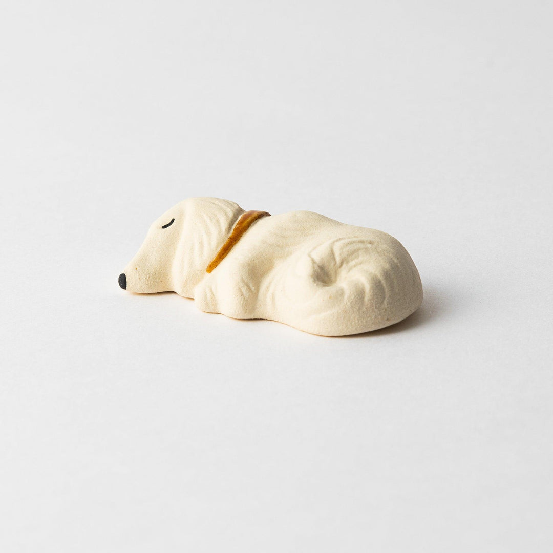 Side view of a white ceramic chopstick rest shaped like a sleeping dog, showing its detailed contours and gold collar.
