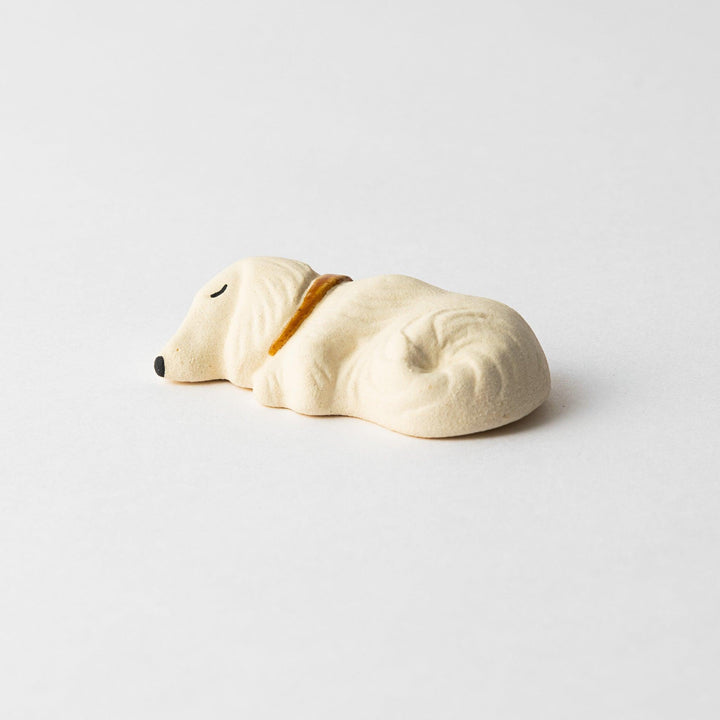 Side view of a white ceramic chopstick rest shaped like a sleeping dog, showing its detailed contours and gold collar.