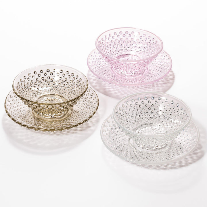 Textured glass dessert bowl and saucer sets in pink, amber, and clear, each with raised dot patterns and a radiant base design.