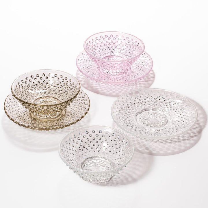 Textured glass dessert bowl and saucer sets in pink, amber, and clear, each with raised dot patterns and a radiant base design.