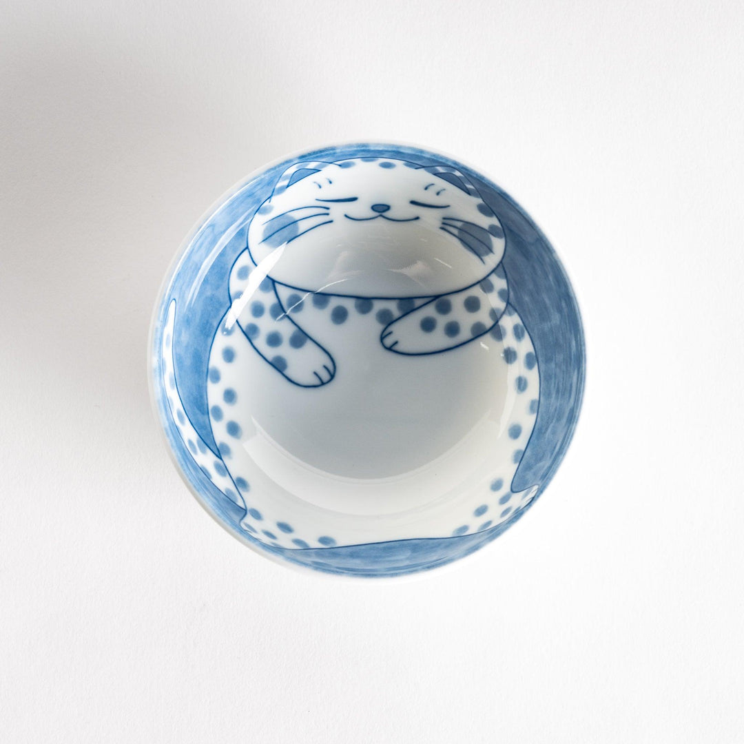 A dessert bowl with a chubby blue-spotted cat, looking peaceful and content.