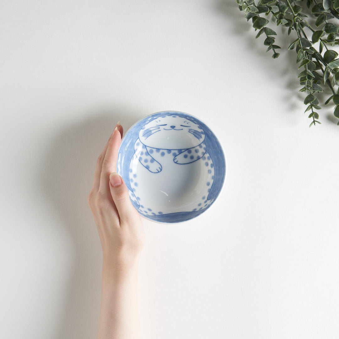 A dessert bowl with a chubby blue-spotted cat, looking peaceful and content.