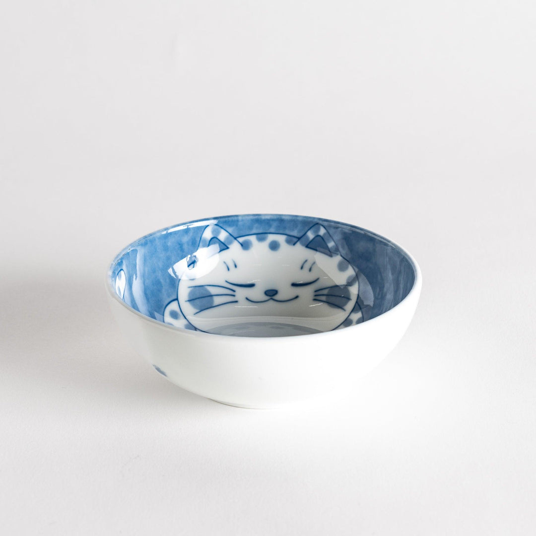 A dessert bowl with a chubby blue-spotted cat, looking peaceful and content.
