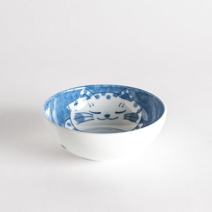 A dessert bowl with a chubby blue-spotted cat, looking peaceful and content.