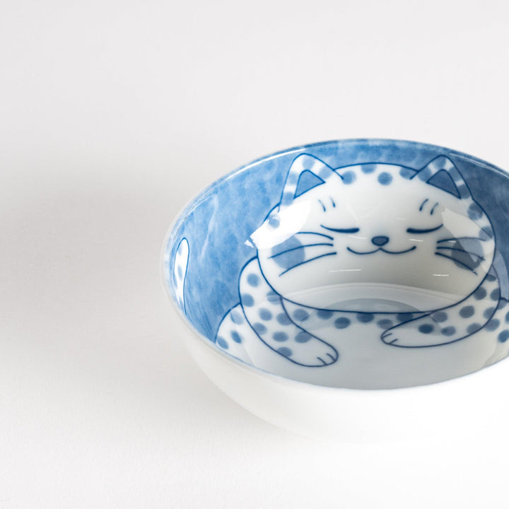 A dessert bowl with a chubby blue-spotted cat, looking peaceful and content.